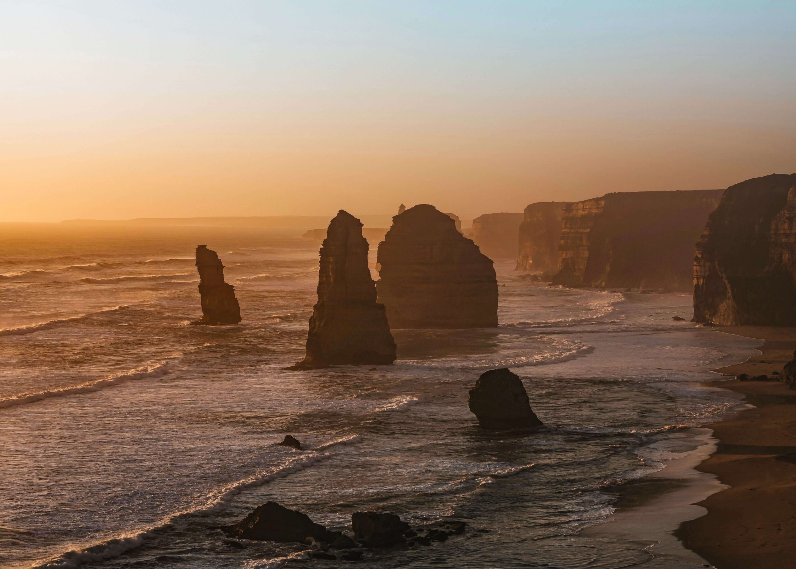 Các cột đá vôi Twelve Apostles trên Great Ocean Road dưới ánh hoàng hôn vàng rực bên bờ biển nước Úc.